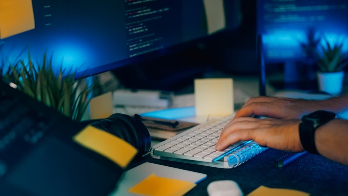 Developer workstation with multiple monitors and code in blue-lit environment.