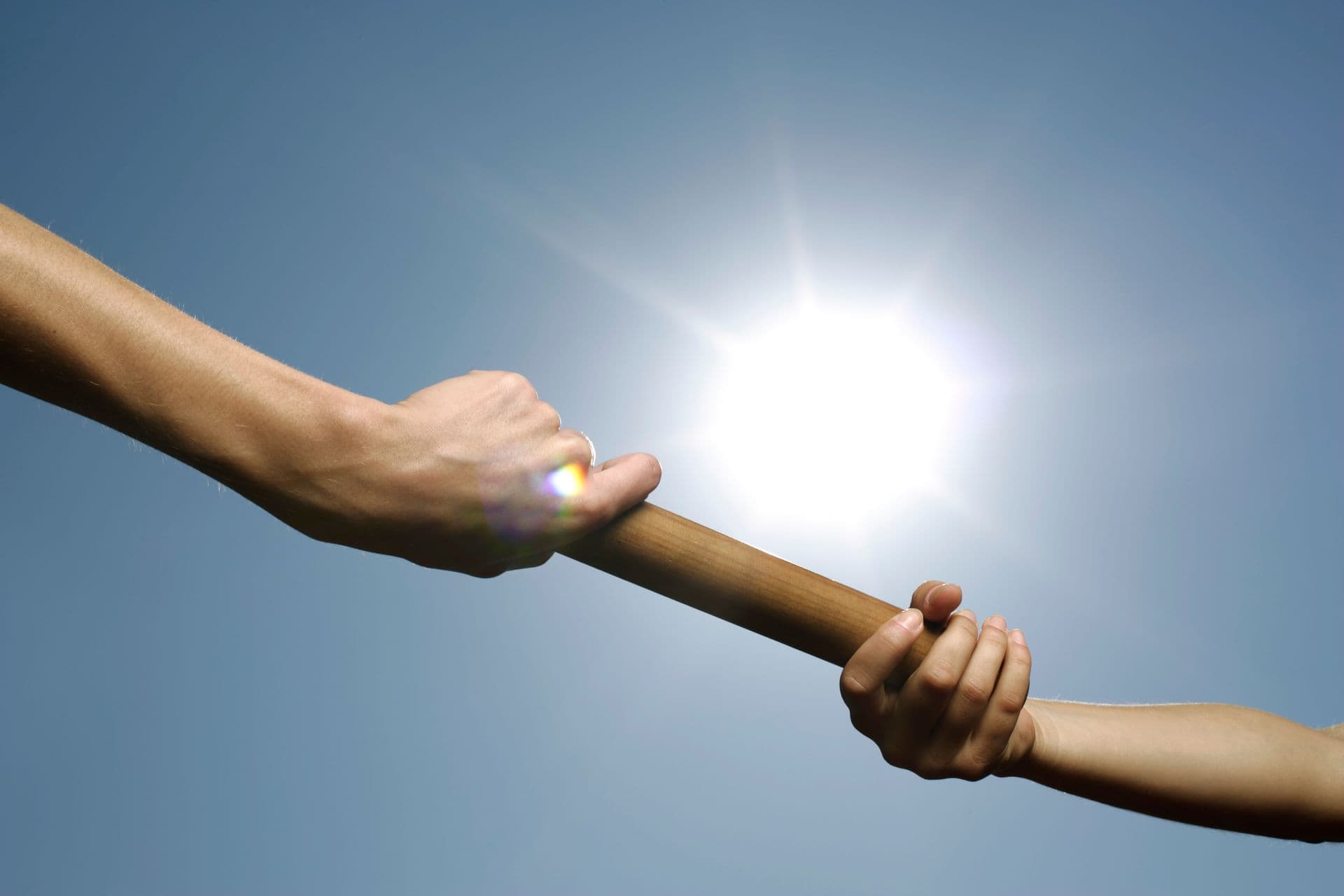 Relay baton being passed between two hands against a bright sky, representing the critical marketing-to-sales handoff.