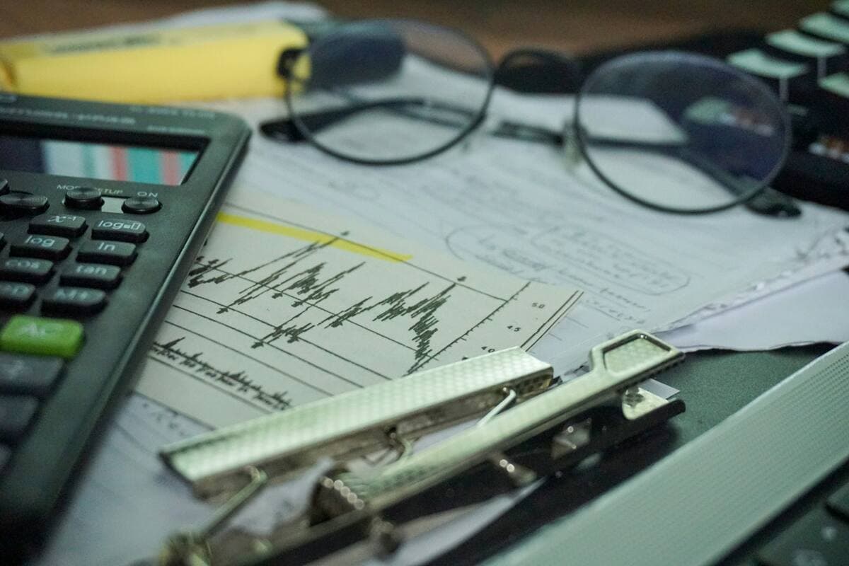 Calculator, printed financial charts and reading glasses on a finance desk during month-end review.